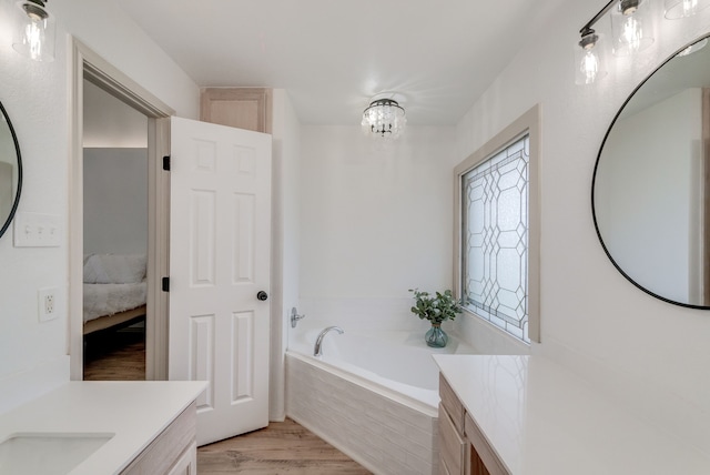 bathroom with hardwood / wood-style flooring, a relaxing tiled tub, vanity, and a notable chandelier