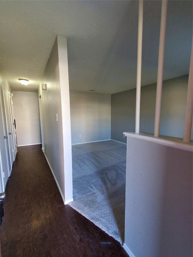 hall with a textured ceiling and dark wood-type flooring