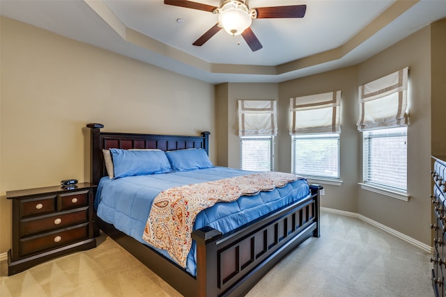 bedroom with ceiling fan, light colored carpet, and a tray ceiling