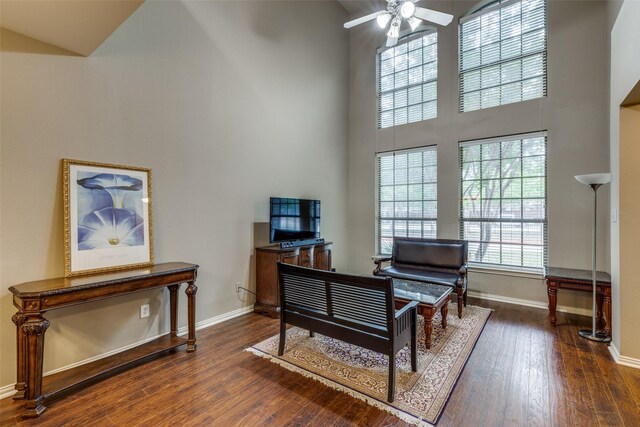 sitting room with ceiling fan, dark hardwood / wood-style flooring, and a towering ceiling