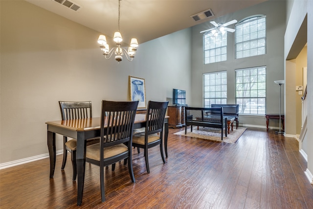 dining area with a towering ceiling, ceiling fan with notable chandelier, and dark hardwood / wood-style floors