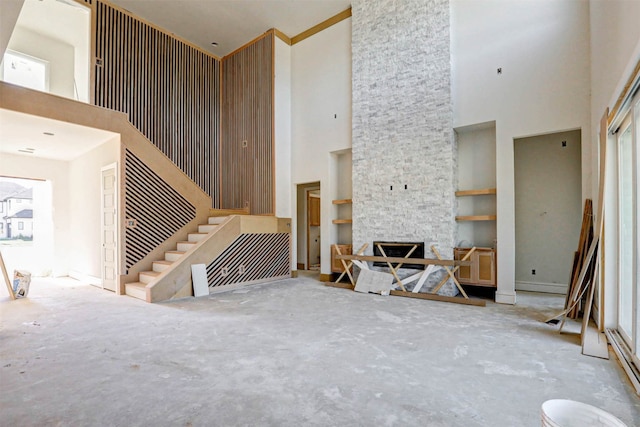 living room featuring built in shelves, a stone fireplace, and a towering ceiling