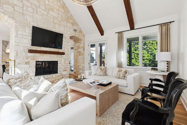 living room featuring beam ceiling, light hardwood / wood-style flooring, a stone fireplace, high vaulted ceiling, and french doors