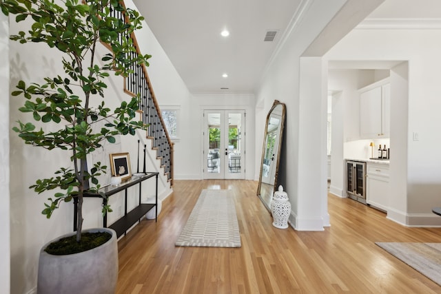 entrance foyer with wine cooler, crown molding, light hardwood / wood-style floors, and french doors