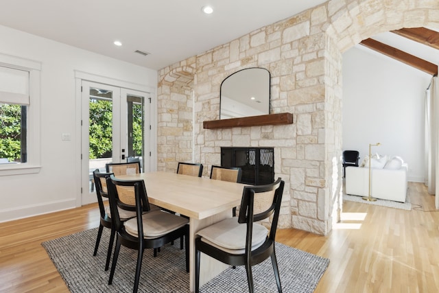 dining area with a stone fireplace, light hardwood / wood-style floors, and french doors