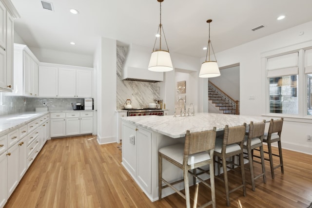 kitchen featuring premium range hood, an island with sink, a breakfast bar area, white cabinets, and light stone countertops