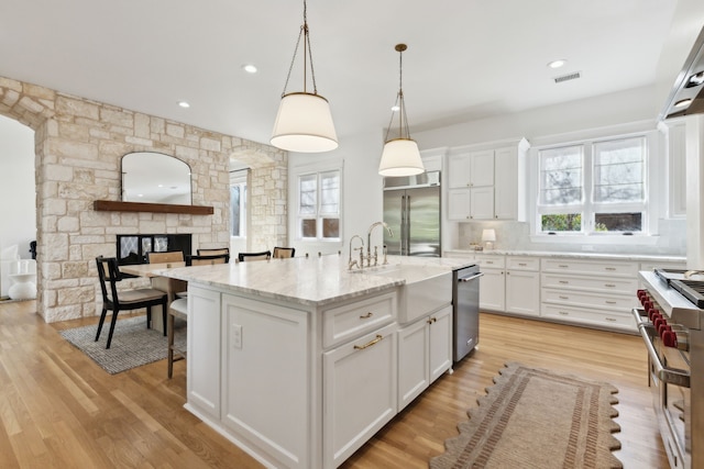 kitchen with a healthy amount of sunlight, high end appliances, visible vents, and white cabinets