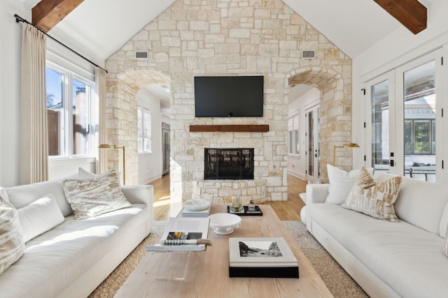 living room featuring wood-type flooring, french doors, a stone fireplace, and lofted ceiling with beams