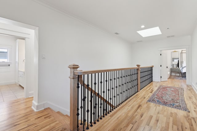 corridor with crown molding, a skylight, and light wood-type flooring