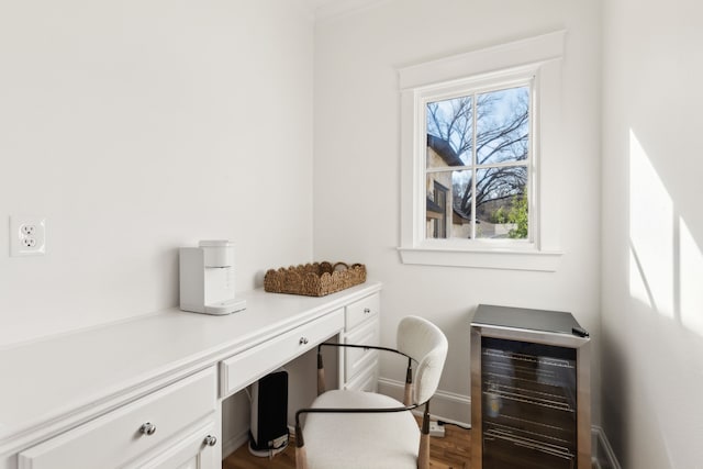 office featuring beverage cooler, baseboards, built in desk, and wood finished floors