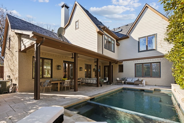 back of property featuring a chimney, outdoor lounge area, central AC unit, a patio area, and an outdoor pool