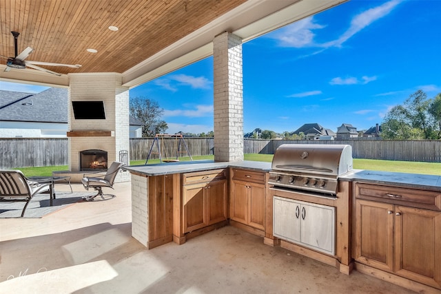 view of patio / terrace featuring ceiling fan, an outdoor kitchen, a playground, area for grilling, and an outdoor brick fireplace