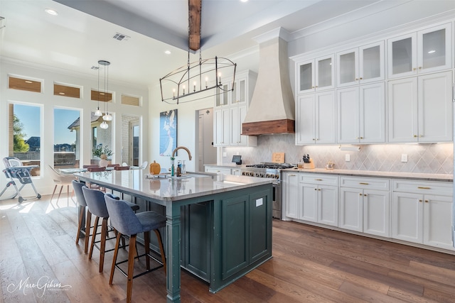 kitchen featuring pendant lighting, a center island with sink, white cabinets, high end stainless steel range oven, and custom range hood