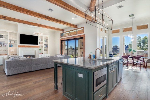 kitchen with pendant lighting, hardwood / wood-style floors, stainless steel microwave, sink, and an island with sink