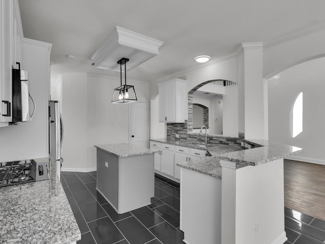 kitchen with kitchen peninsula, light stone countertops, stainless steel appliances, a center island, and white cabinetry