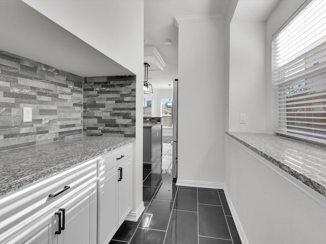 kitchen with decorative backsplash, light stone countertops, dark tile patterned floors, white cabinets, and stainless steel refrigerator