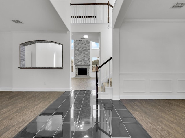 foyer with a stone fireplace, wood finished floors, visible vents, and crown molding