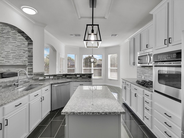 kitchen with backsplash, stainless steel appliances, sink, white cabinetry, and a kitchen island