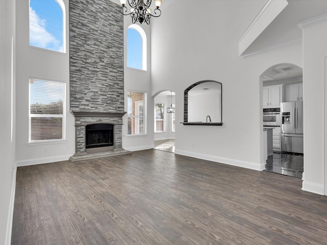 unfurnished living room featuring arched walkways, a stone fireplace, dark wood-style flooring, baseboards, and an inviting chandelier