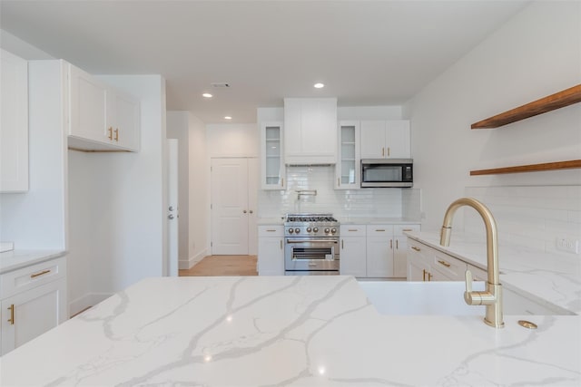 kitchen with backsplash, light stone counters, custom range hood, stainless steel appliances, and white cabinetry