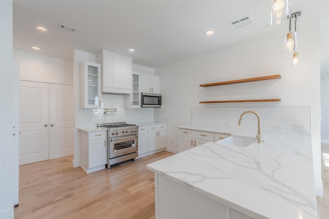 kitchen featuring appliances with stainless steel finishes, light stone counters, decorative light fixtures, light hardwood / wood-style floors, and white cabinetry