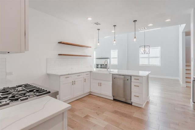 kitchen with kitchen peninsula, hanging light fixtures, light hardwood / wood-style flooring, white cabinetry, and stainless steel appliances