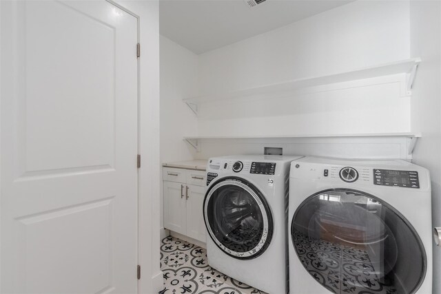 clothes washing area featuring cabinets, light tile patterned floors, and washing machine and clothes dryer