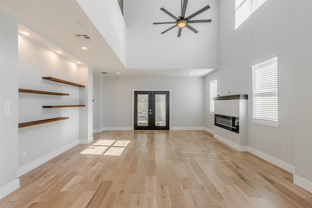 unfurnished living room featuring ceiling fan, french doors, light hardwood / wood-style floors, and a high ceiling