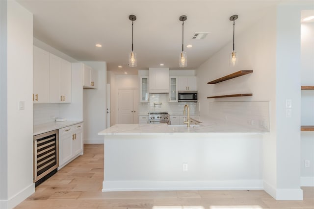 kitchen featuring white cabinets, light wood-type flooring, appliances with stainless steel finishes, decorative light fixtures, and beverage cooler