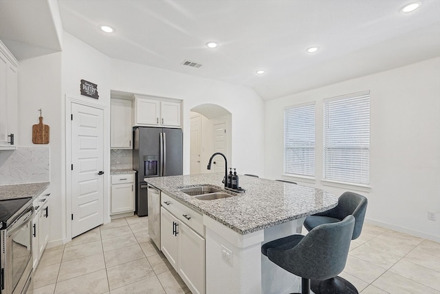 kitchen featuring light stone countertops, sink, backsplash, an island with sink, and white cabinets