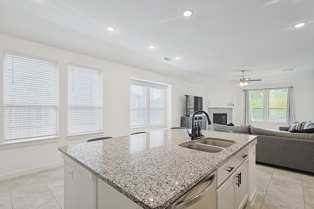 kitchen featuring light stone countertops, white cabinetry, sink, stainless steel dishwasher, and a kitchen island with sink