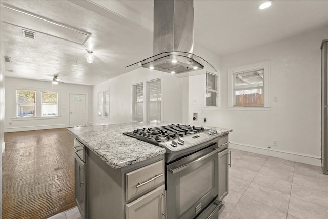 kitchen with island range hood, visible vents, baseboards, open floor plan, and stainless steel range with gas cooktop