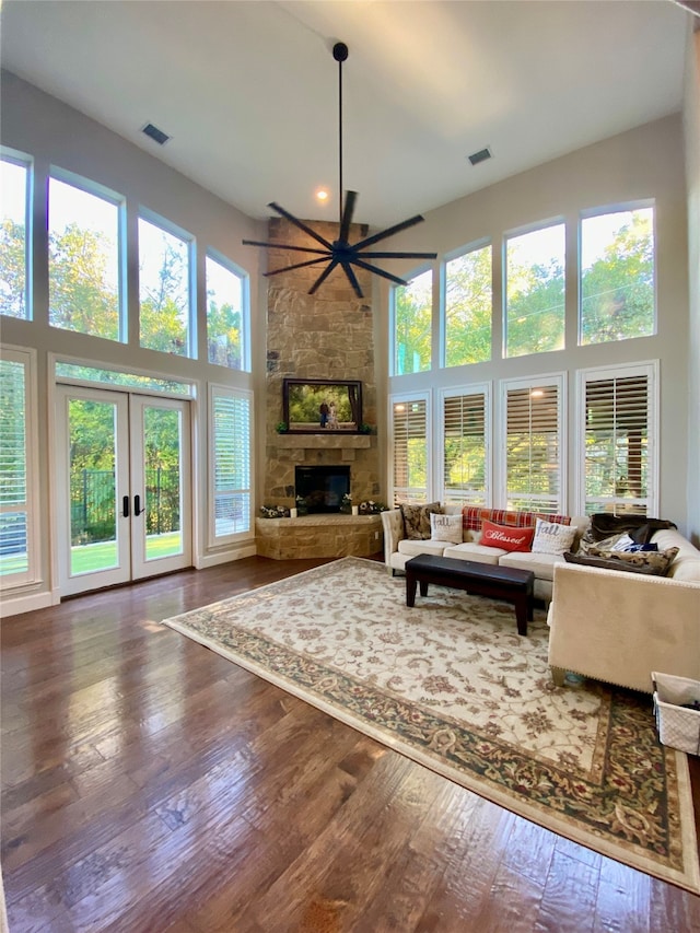 living room with french doors, hardwood / wood-style flooring, ceiling fan, a towering ceiling, and a fireplace