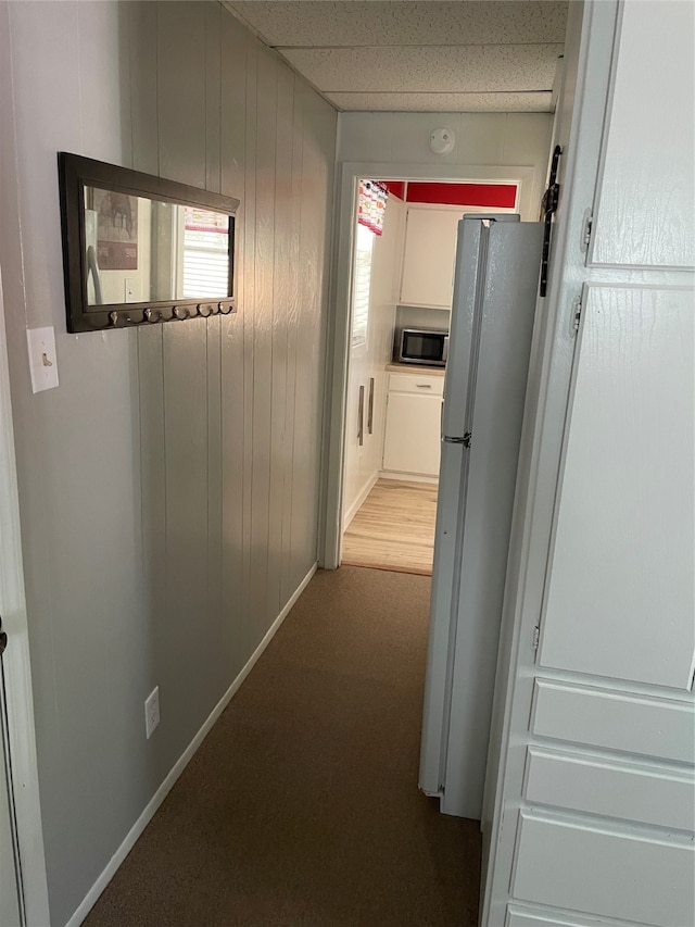 corridor with a paneled ceiling, carpet flooring, and wood walls