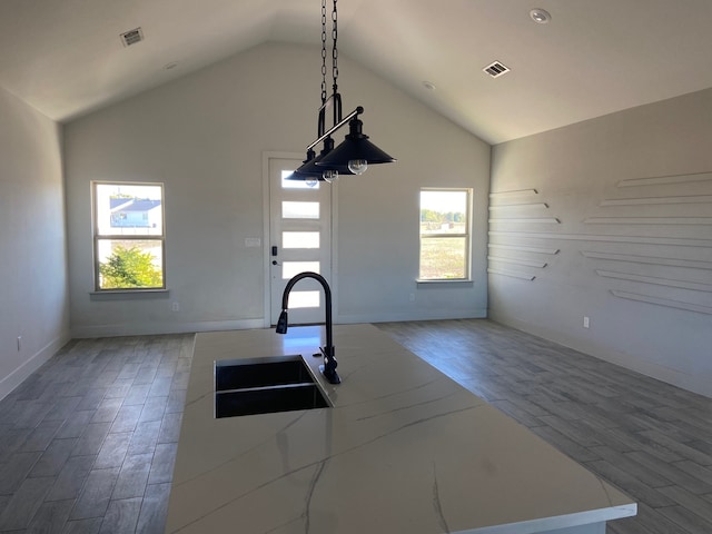 interior space featuring a kitchen island with sink, sink, hanging light fixtures, vaulted ceiling, and wood-type flooring