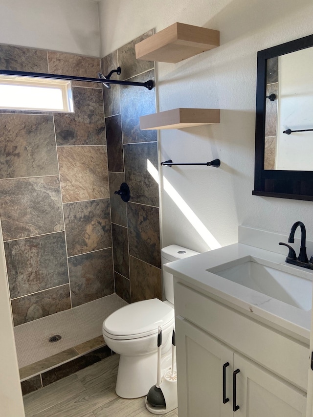 bathroom with toilet, hardwood / wood-style floors, vanity, and tiled shower