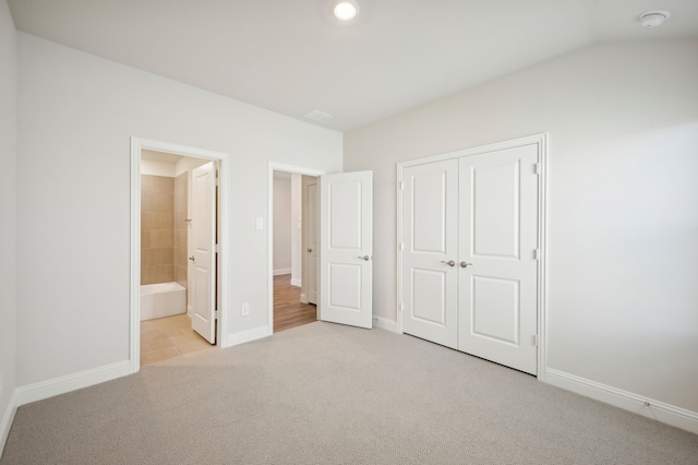 unfurnished bedroom with lofted ceiling, light carpet, connected bathroom, and a closet