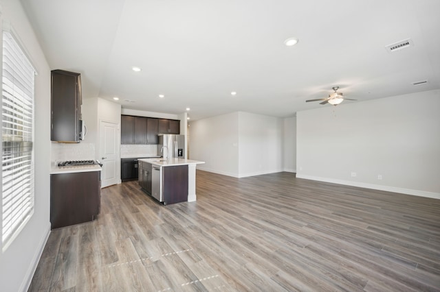 kitchen with appliances with stainless steel finishes, tasteful backsplash, a kitchen island with sink, ceiling fan, and hardwood / wood-style flooring