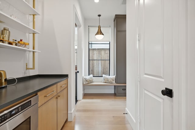 bar featuring light brown cabinets, light hardwood / wood-style flooring, pendant lighting, and stainless steel oven