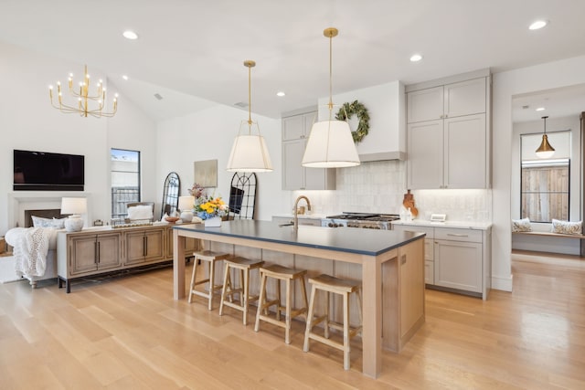 kitchen featuring sink, tasteful backsplash, an island with sink, lofted ceiling, and decorative light fixtures