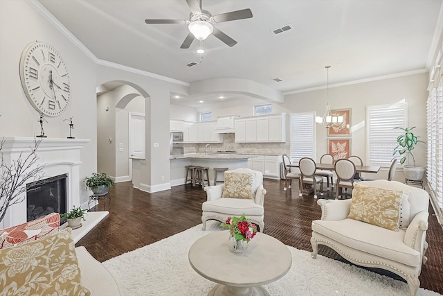 living room featuring crown molding, dark wood-type flooring, and ceiling fan with notable chandelier