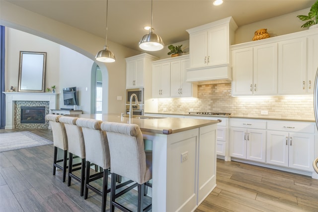 kitchen featuring white cabinets, a center island with sink, sink, decorative light fixtures, and light hardwood / wood-style floors