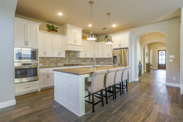 kitchen with a kitchen island with sink, white cabinets, hanging light fixtures, dark hardwood / wood-style flooring, and stainless steel appliances