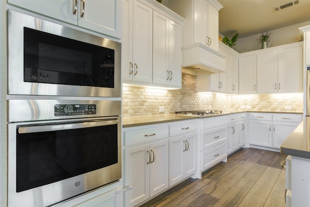 kitchen with white cabinets, appliances with stainless steel finishes, light wood-type flooring, and decorative backsplash