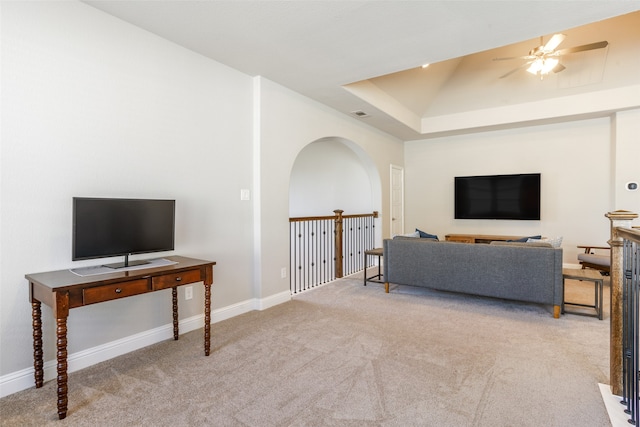 carpeted living room with a raised ceiling and ceiling fan