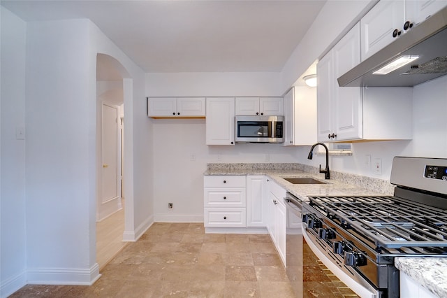 kitchen with white cabinets, appliances with stainless steel finishes, light stone countertops, and sink