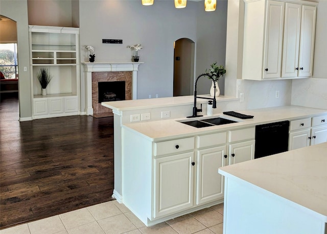 kitchen with sink, a tile fireplace, light hardwood / wood-style flooring, white cabinets, and black dishwasher