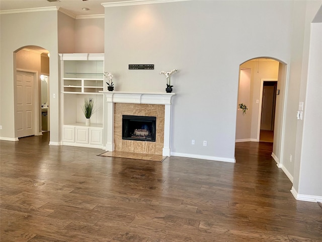 unfurnished living room featuring crown molding, a fireplace, a towering ceiling, and dark wood-type flooring