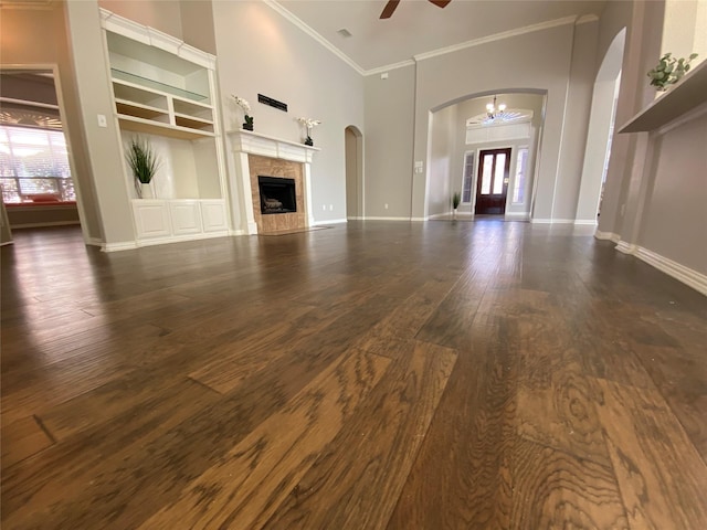 unfurnished living room with plenty of natural light, dark hardwood / wood-style flooring, crown molding, and a tiled fireplace