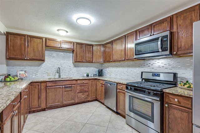 kitchen featuring appliances with stainless steel finishes, light stone counters, a textured ceiling, sink, and light tile patterned floors